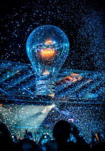 Cirque Bijou - Muse Stadium Tour - Giant lightbulb flies above audience with aerialist hanging from it, confetti fills the air
