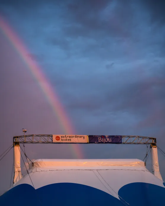 A rainbow hits two signs on top of a Big Top - Extraordinary Bodies and Cirque Bijou