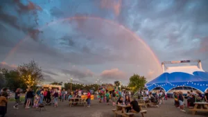 A picture of a blue Big Top with people gathered outside, fairy lights and a rainbow