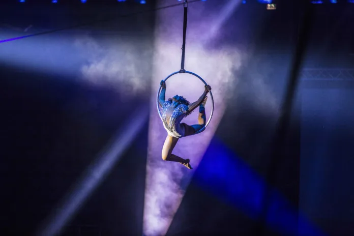 An aerialist hangs suspended in her aerial hoop, with purple lighting and smoke surrounding her