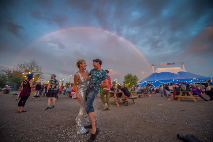 Two people embrace smiling at each other, with a rainbow and big top in the background