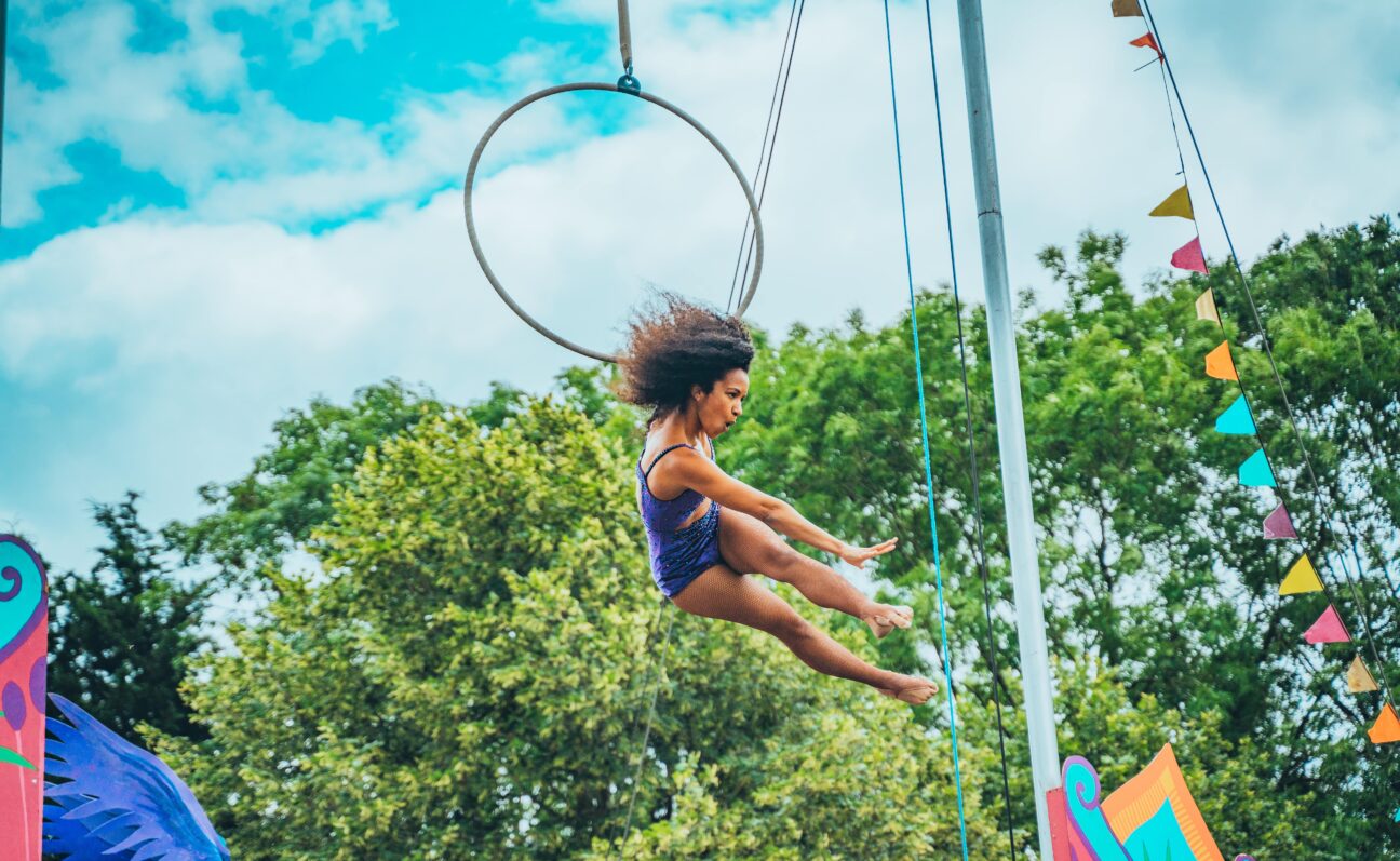 An aerialist swings from her hoop, reaching towards the crowd