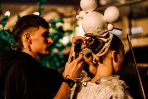 A stage manager assists one of the performers with her elaborate head piece before a show