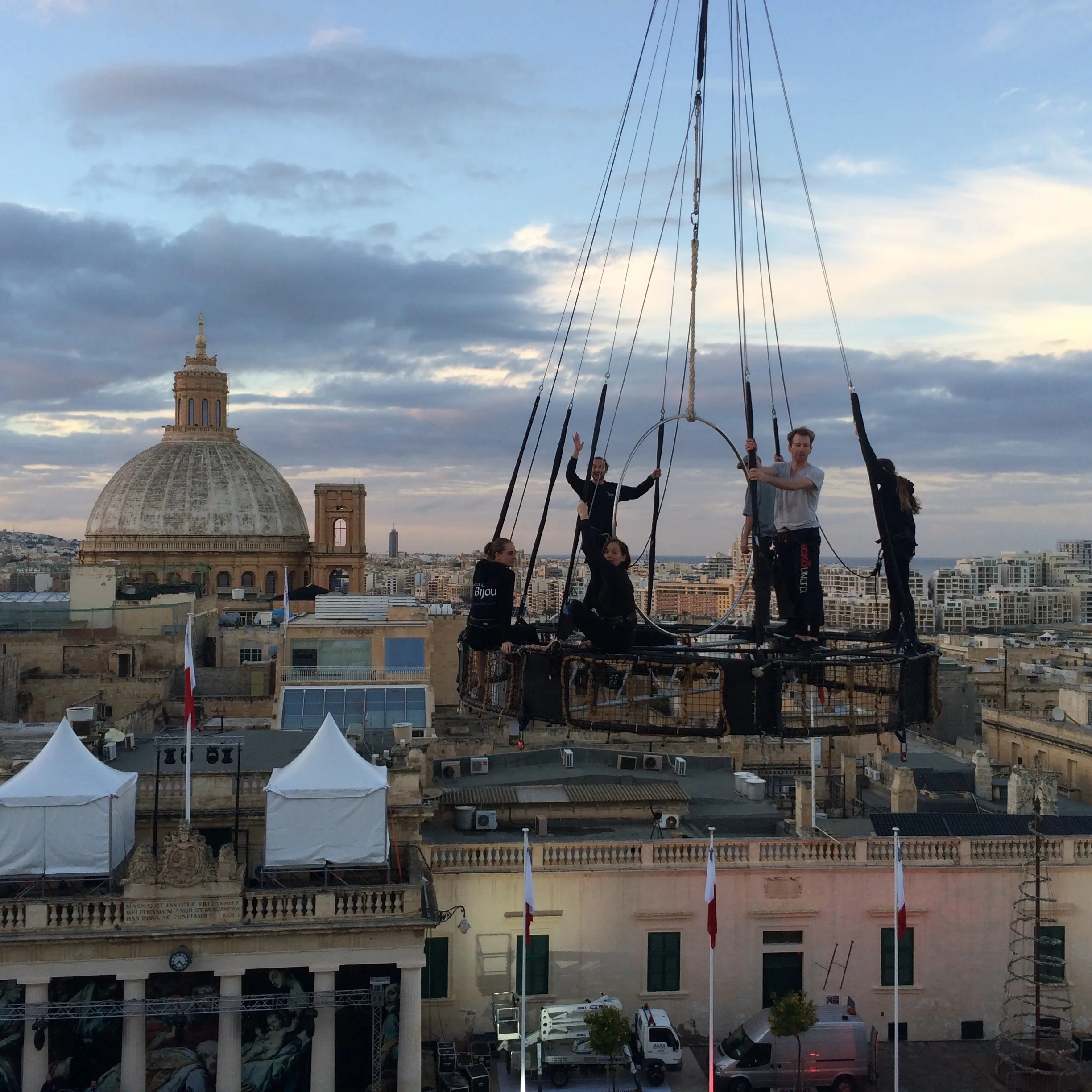 Picture of daners standing on an aerial crane ring with Malta cityscape in the background