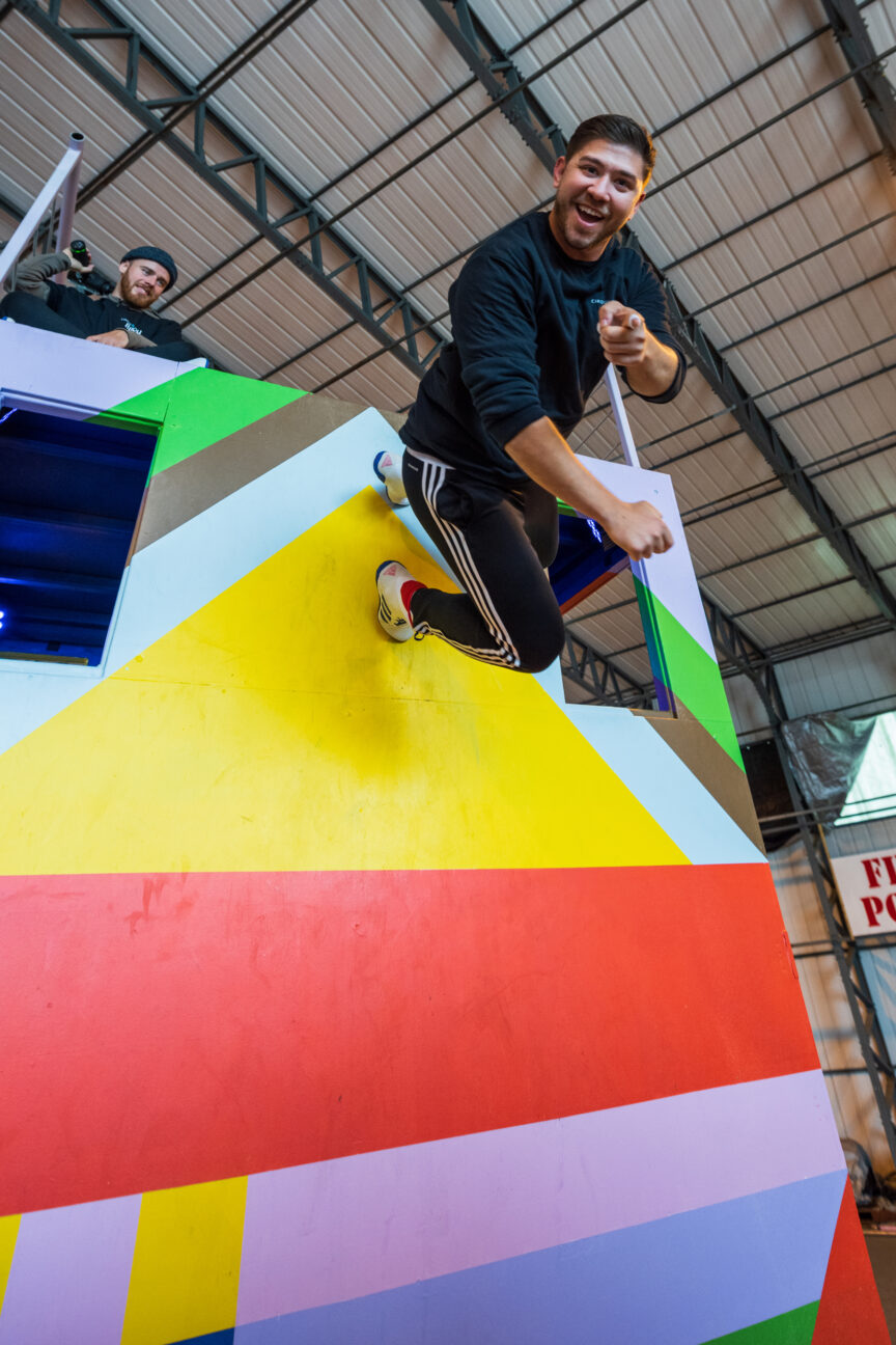 A trampwall artist bounces on a trampoline, pointing and smiling to camera