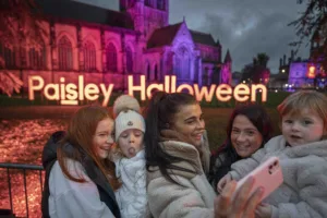 A family gather together to take a selfie in front of the illuminated Paisley Abbey, with large led letters that read Paisley Halloween