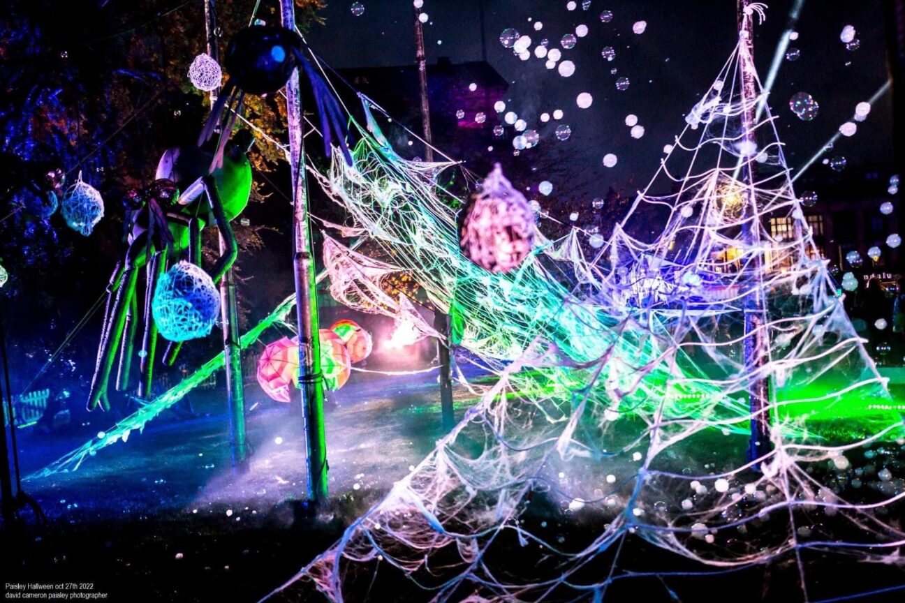 A spider web with bubbles, lit with lots of different colours