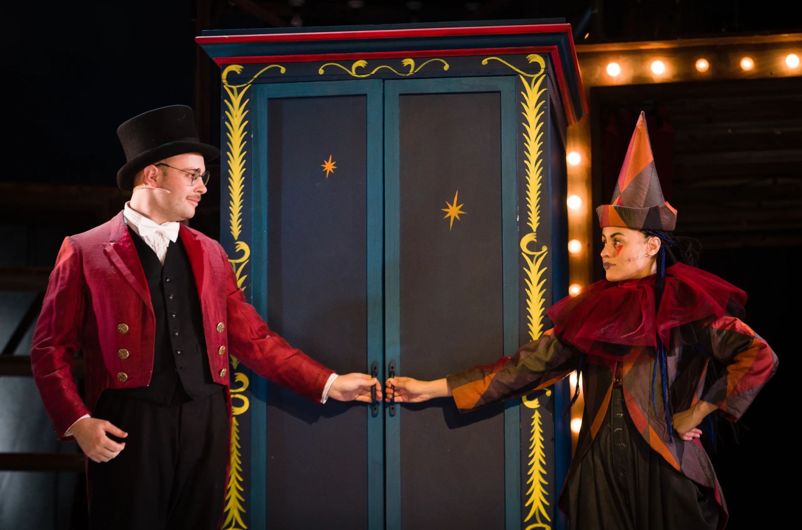 Two performers - one dressed in circus gear and one dressed as a clown stand either side of a cupboard door, ready to open it