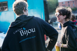 Two crew members smile at each other. Cirque Bijou callout for Stage Managers and Show Callers