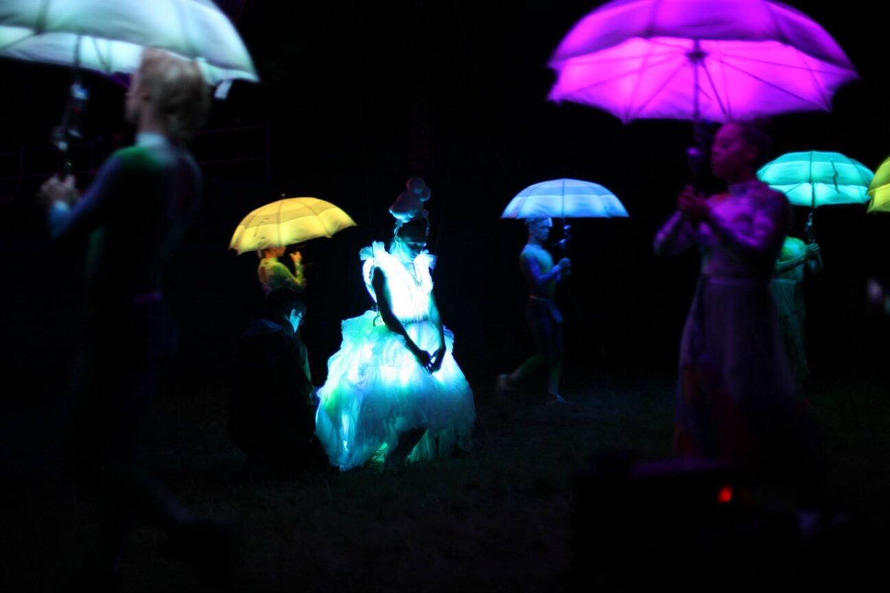 A performer stands poised in Cirque Bijous led dress, surrounded by our led umbrellas - Goodwood FOS 2015