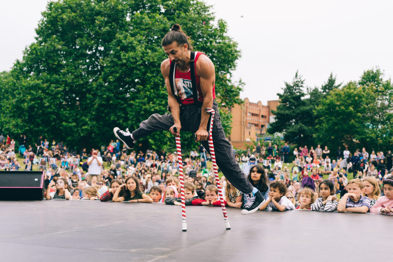 Bristol Harbourside Festival 2016, a performer lifts his legs up and balances on red and white striped crutches.