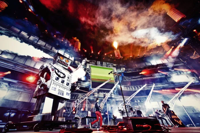 Charles the Robot on stage for the MUSE world tour. He's in front of a big crowd, with lights and smoke and lasers surrounding him