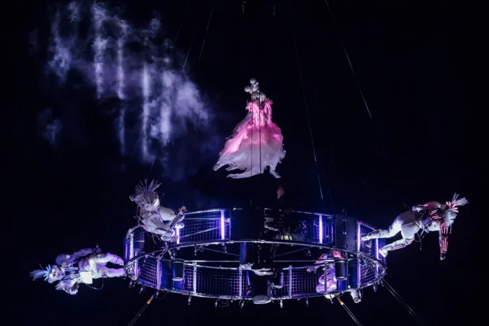 An aerialist in our led dress performs above our aerial carousel, surrounded by four other performers illuminated against the black night sky