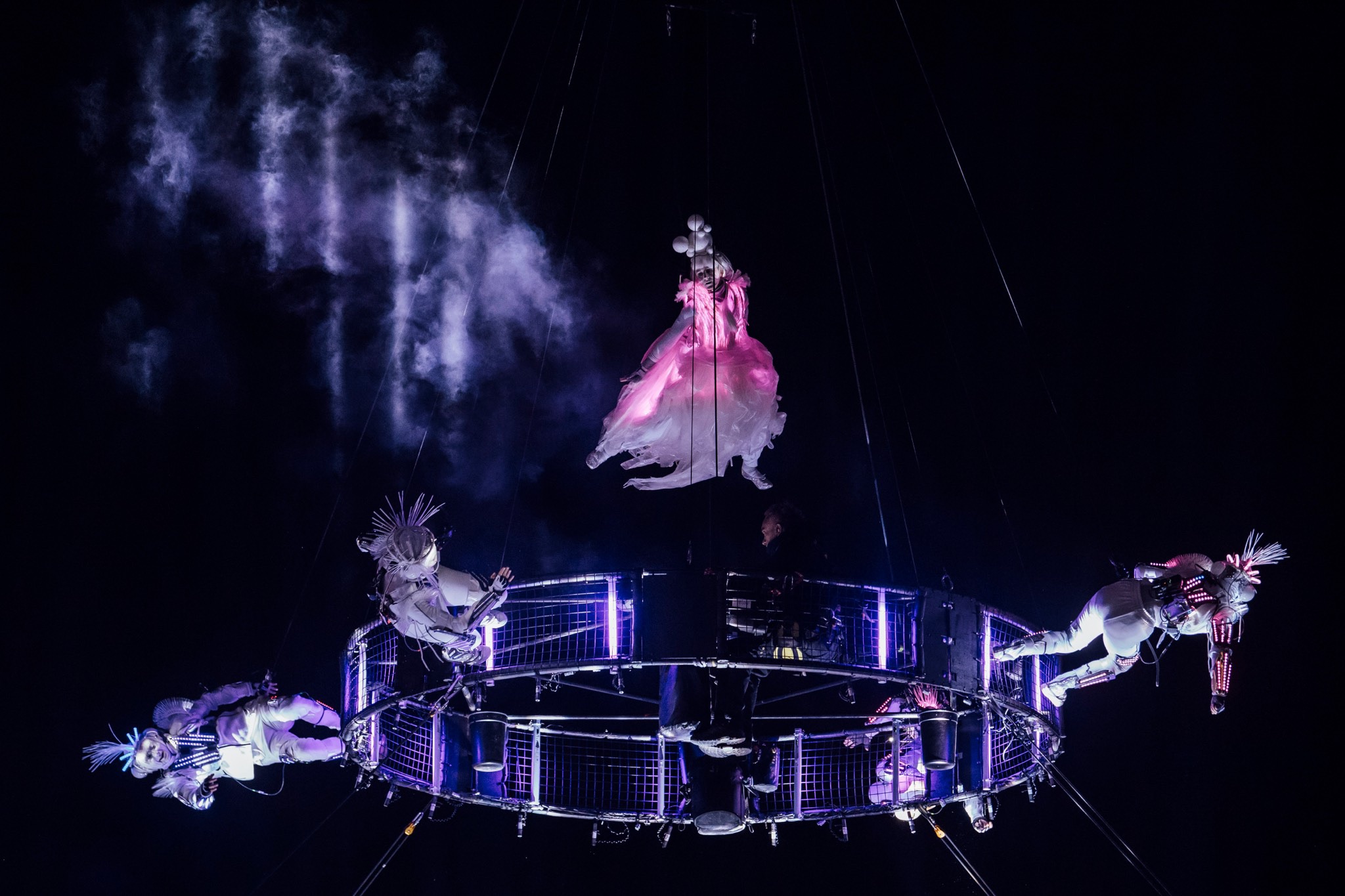 An aerialist in our led dress performs above our aerial carousel, surrounded by four other performers illuminated against the black night sky