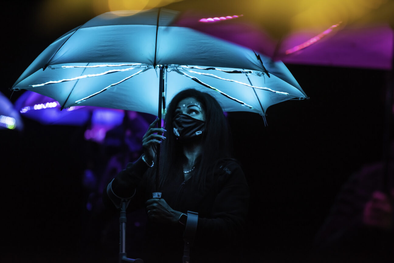 A female performer holds a blue LED umbrella above her head.