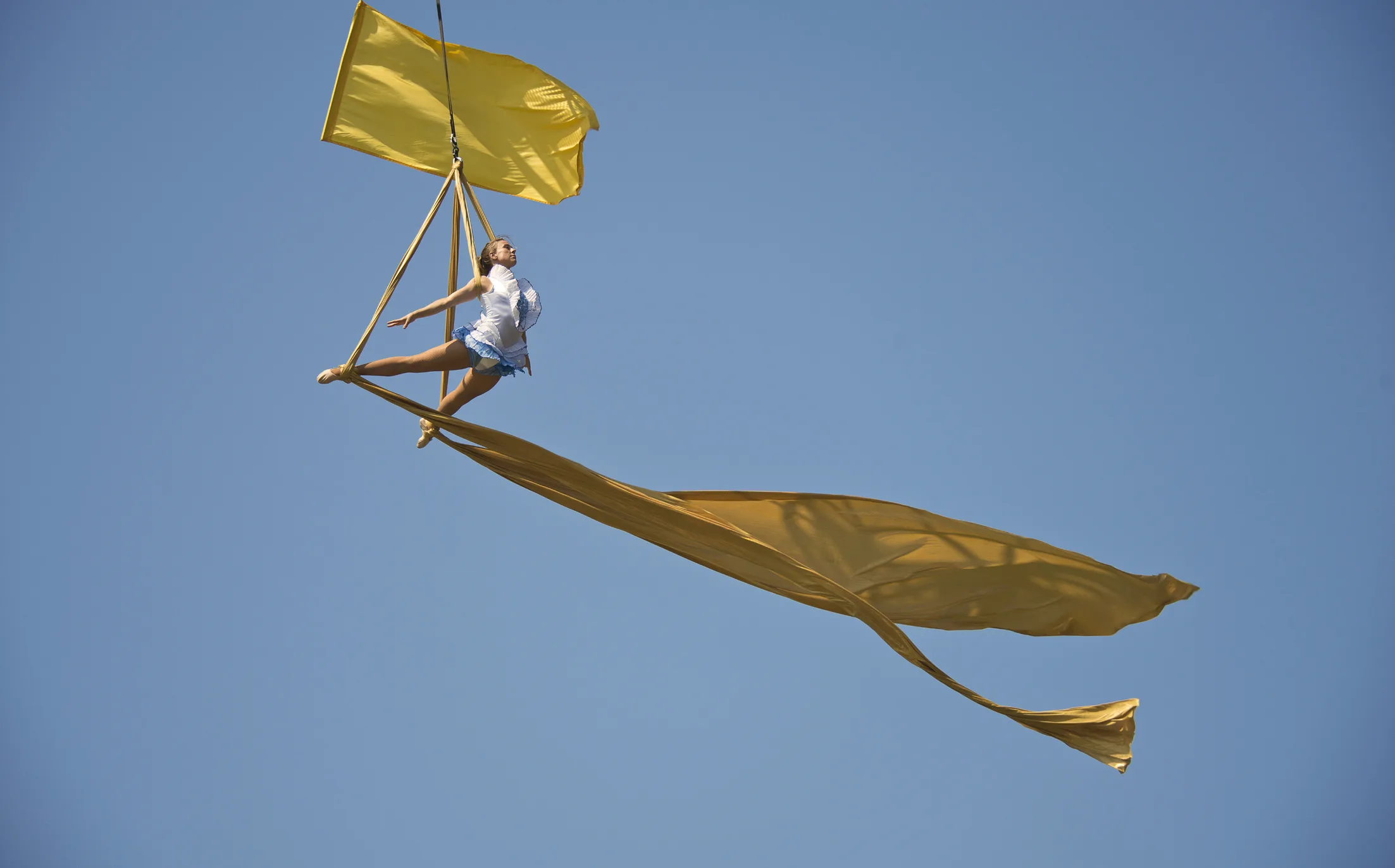 An aerialist poses dramatically against a clear blue sky - yellow flags fly around her