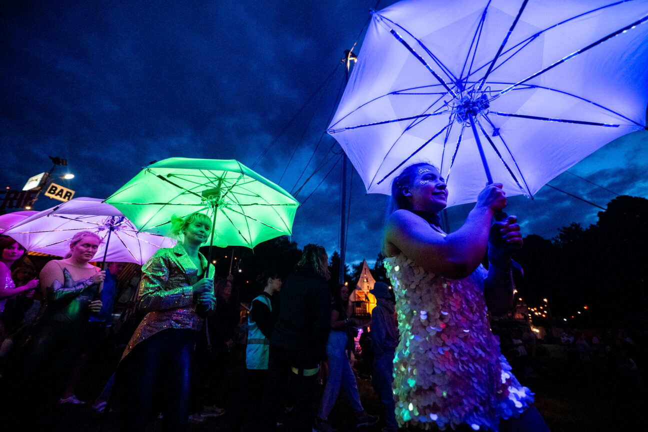 Circomedia students parade with our LED Umbrellas through Camp Bestival Shrophire at night through the crowds