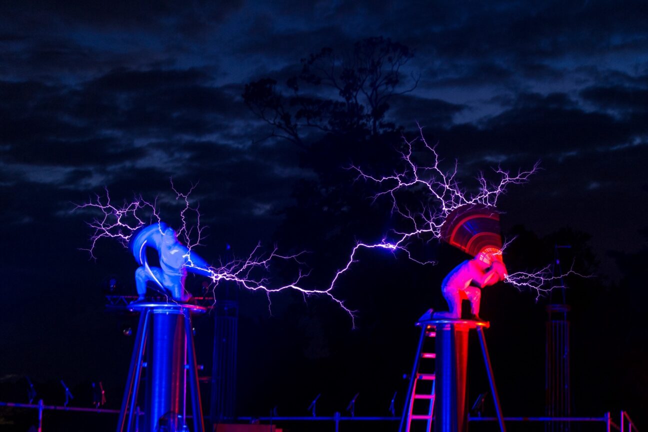 Goodwood Festival of Speed. Two performers, one lit in red and one lit in blue light. The performer on the left strikes the other performer with lightning. They are on raised, circular, metal platforms.