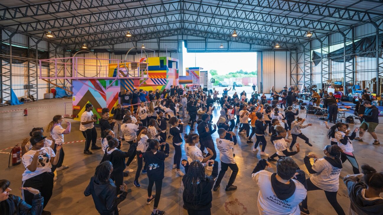 A large number of artists rehearse in a huge aircraft hanger for our Jubilee show, with our colourful float in the background