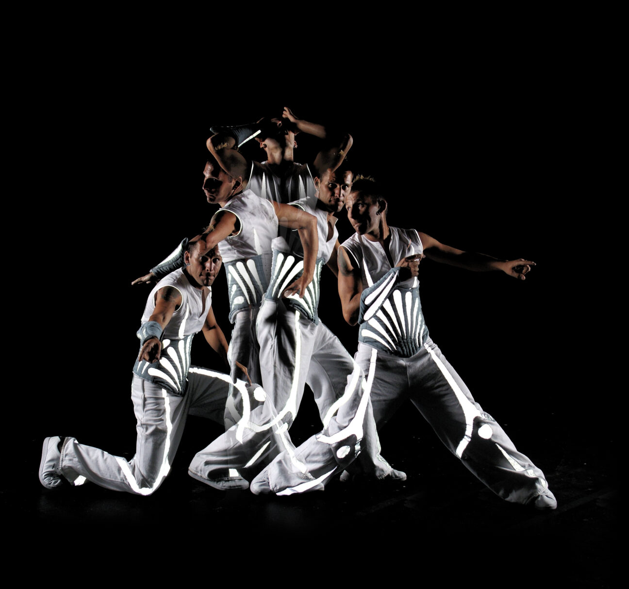 time lapsed shot of an artist striking different poses in a silver and grey costume against a dark background