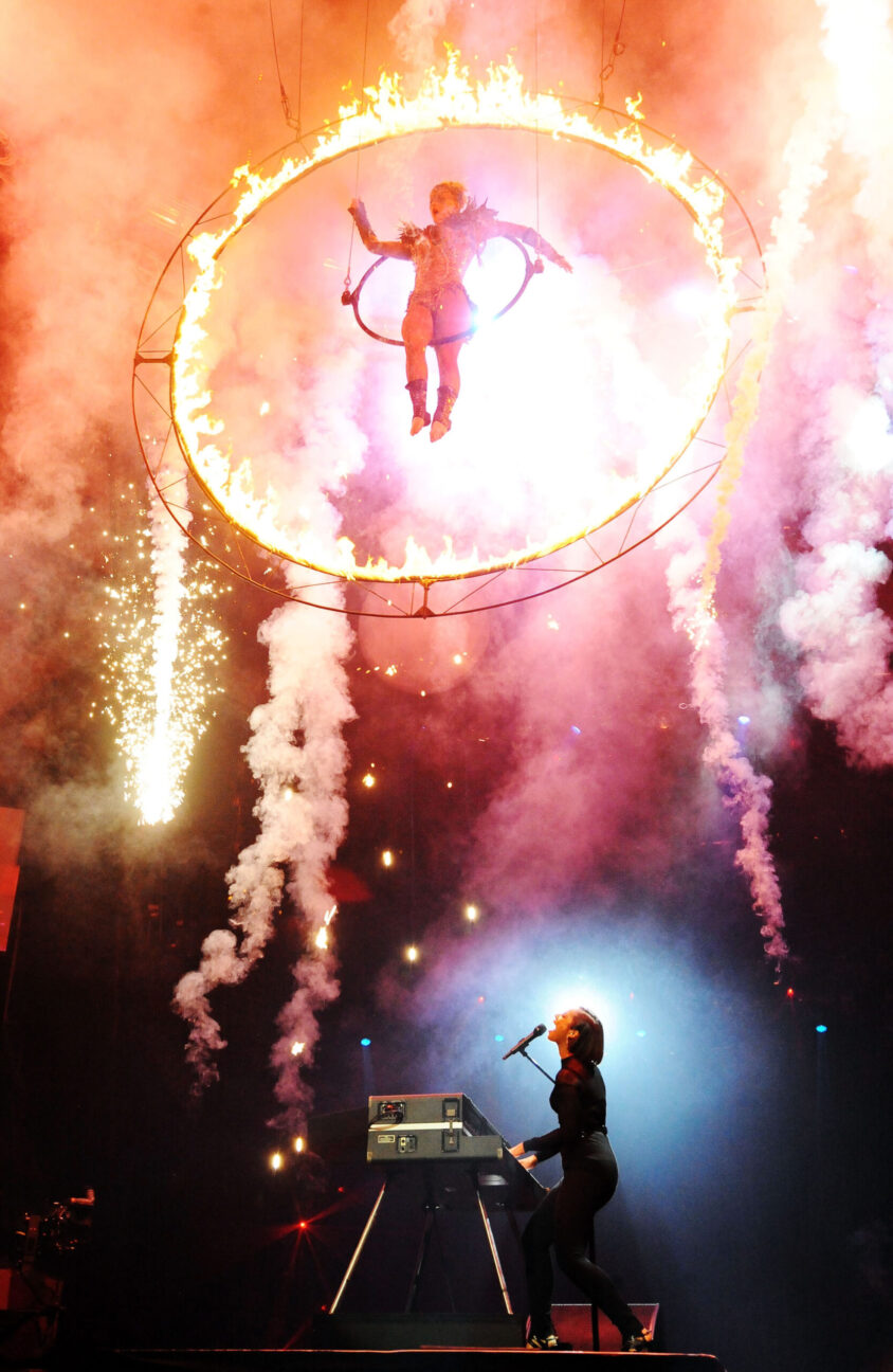 Aerialist suspended in a aerial hoop on fire, performing above Alicia Keys.  Rock and roll touring