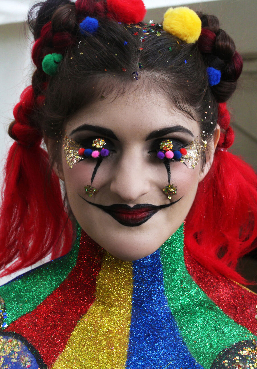 A performer smiles at the camera with her eyes closed - she has full body paint on as a glittery harlequin clown