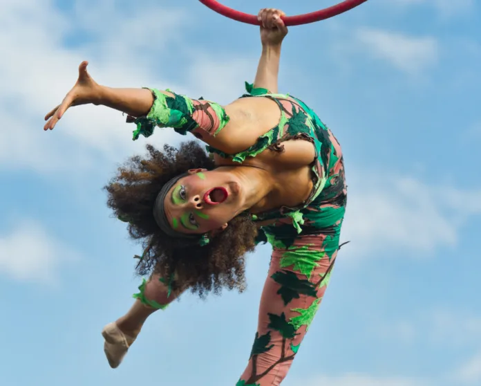 Bristol Harbour Festival- an aerialist hangs from an aerial hoop and looks directly into the camera, mouth open wide and arm stretched out.