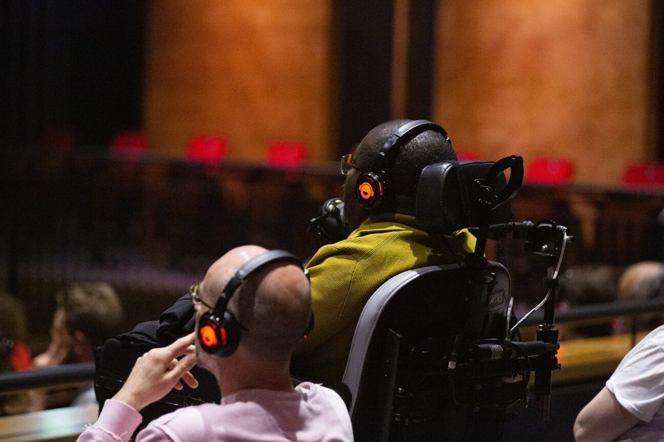 Audience sit captivated by the show, listening to audio description using binaural headsets