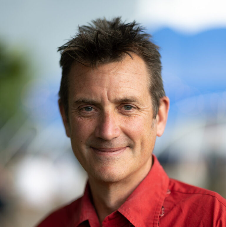 Artistic Director Julian Bracey smiling at the camera in a red collared shirt.