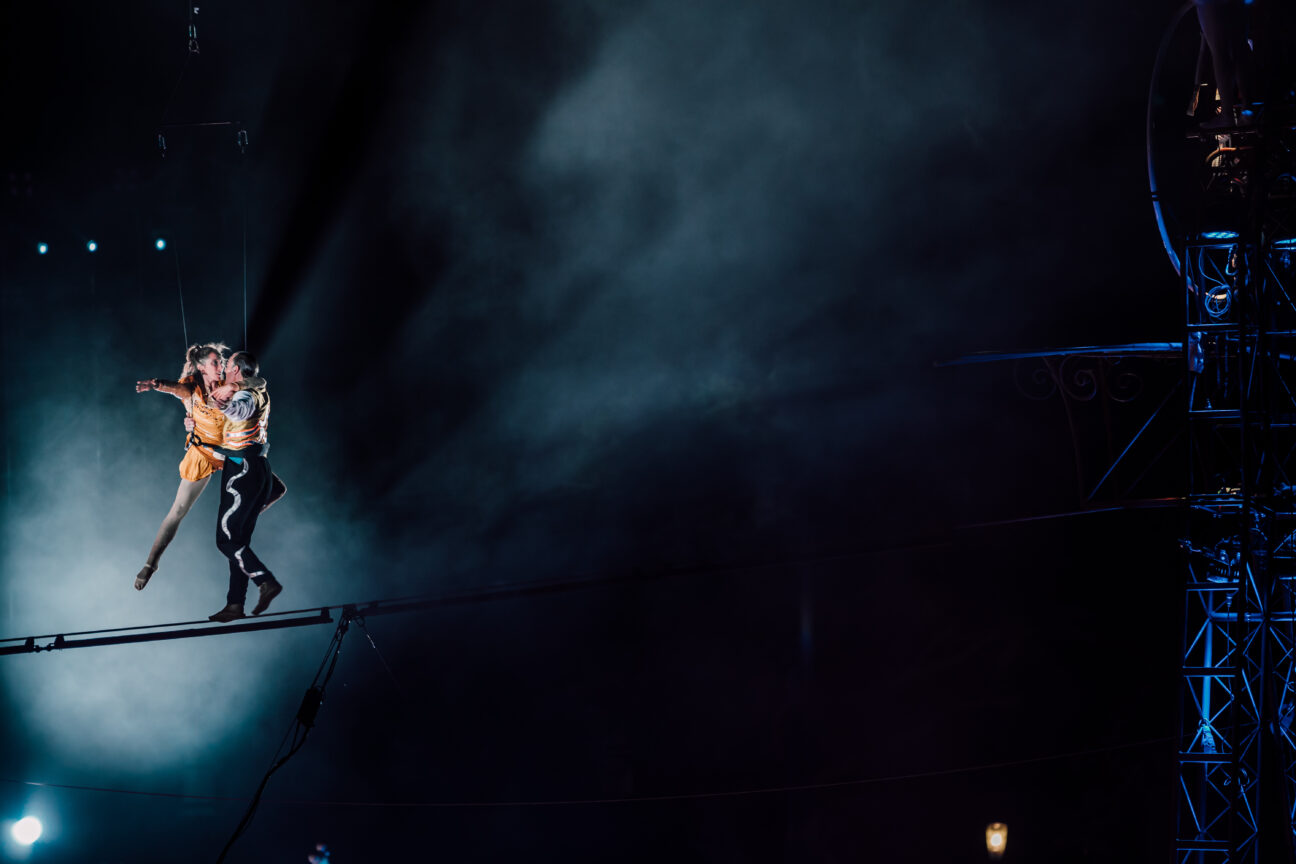 A touching moment between our wire walker and our aerialist, embracing on the high wire against a dark night sky