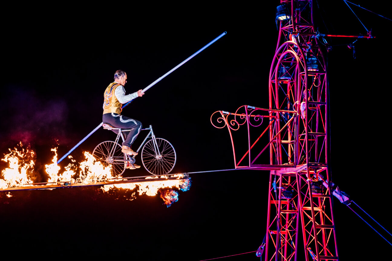 Our wire walker crossing a fiery line on a bicycle