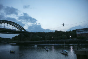 A landscape shot showing the River Weir and Wearmouth Bridge and performer Chris Bullzini walking along the wire. Portolan, Sunderland Tall Ships, Cirque Bijou. Image Dan Prince. 