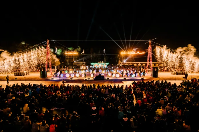 Taiwan Lantern festival, tight wire walkers lit on big metal structure with performers with light up umbrellas below and the audience watching in the foreground of the picture. Pyrotechnics are happening either side of the tight wire.