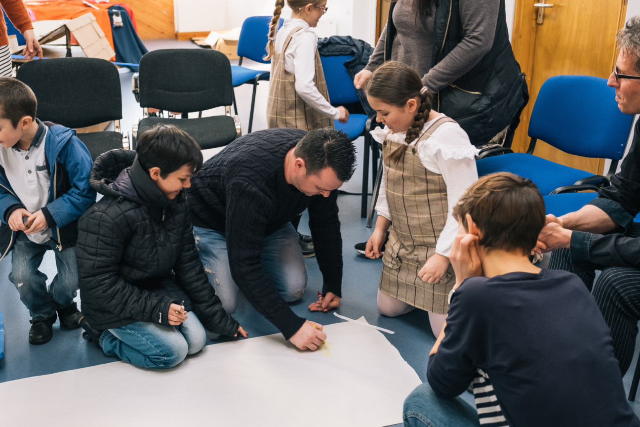 An adult making notes surrounded by kids and other participants at the Kitchen Circus Project.