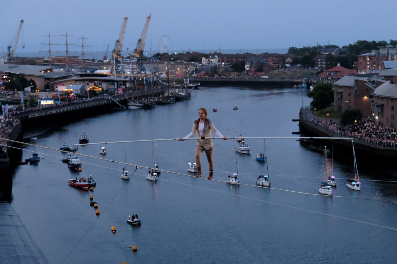 Female wire walker above ships below and audience watching on from a distance.