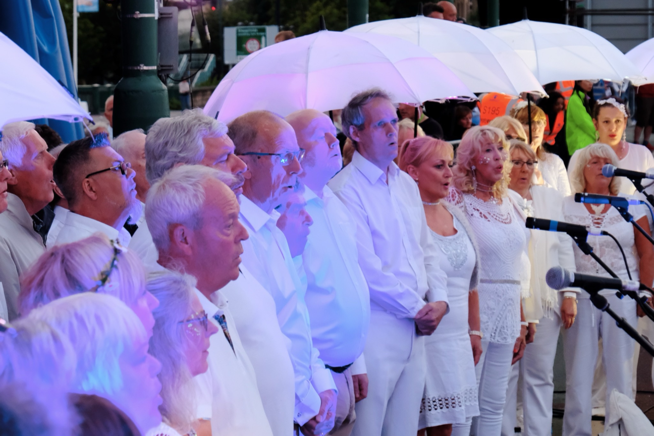 Sunderland Tall Ships. A choir group dressed in white singing into microphones. Some people are standing under white umbrellas.