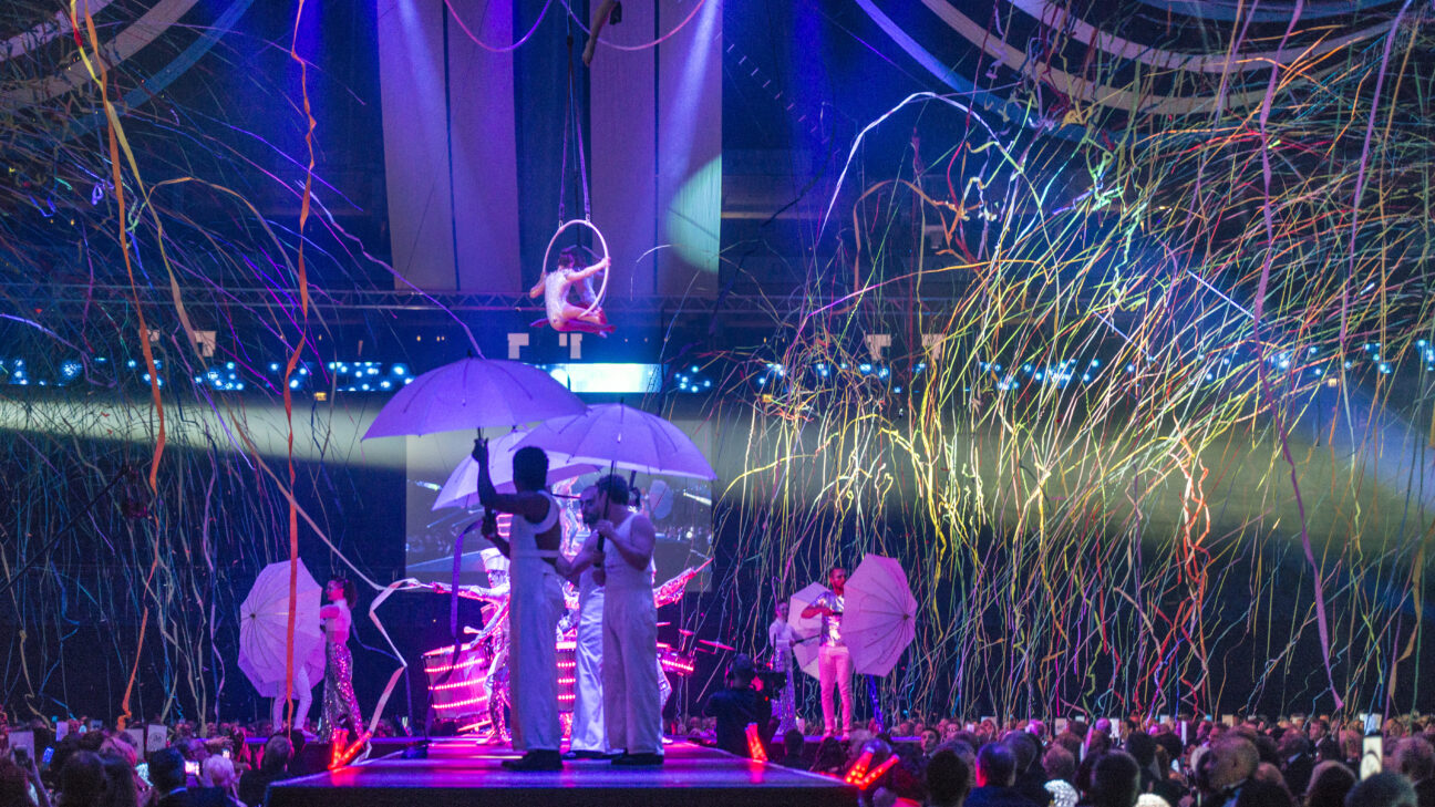 Artists onstage and up in the air perform whilst confetti cannons go off around them