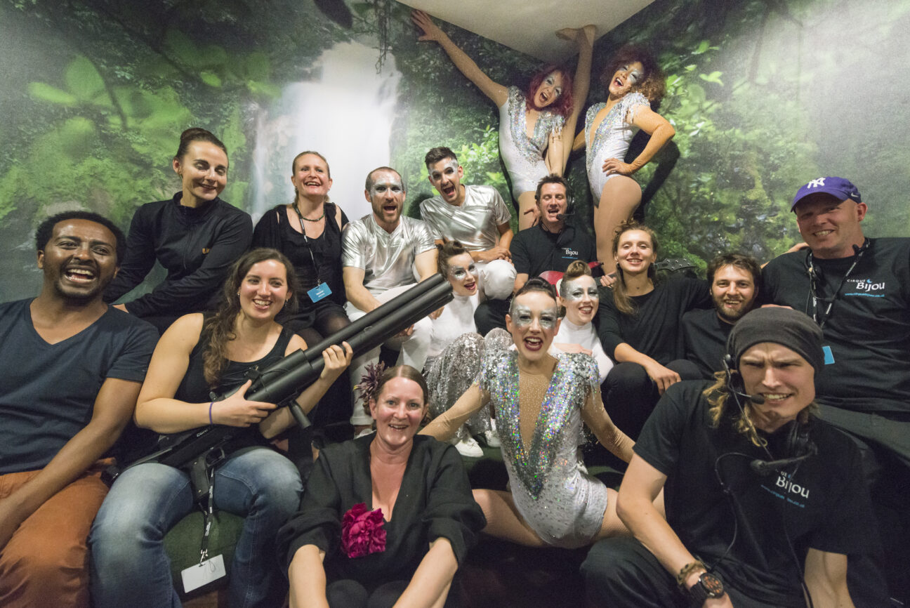 A group shot of cast and crew backstage looking happy and content