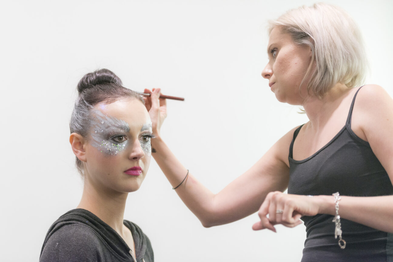 A make up artist puts the finishing touches to one of the performers, who already has beautiful silver make up around her eyes