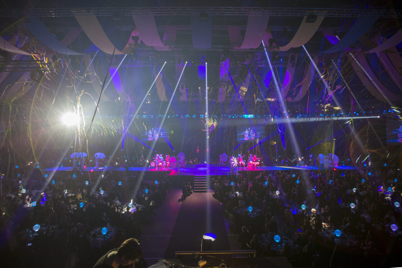 a wide angle shot of the stage, with audience surrounding it and lights on ready for the show to begin