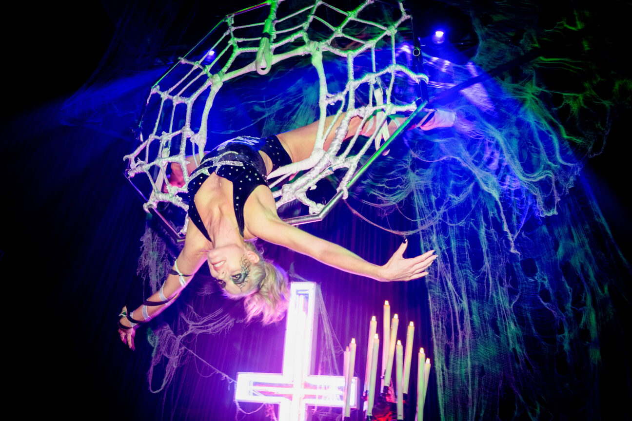 Batman Party aerial performer bending backwards through an aerial hoop that's decorated as a spider's web.