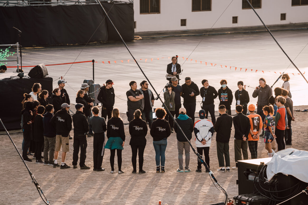 A group of artists and crew stand in a circle facing each other, discussing the show they are creating and sharing ideas