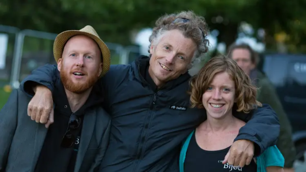 Three people stand hugging and smiling at the camera