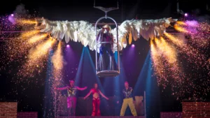 A singer is raised up in a cage, with large wings opened either side of them. Pyrotechnics fire out from the ends of the wings, showering performers below