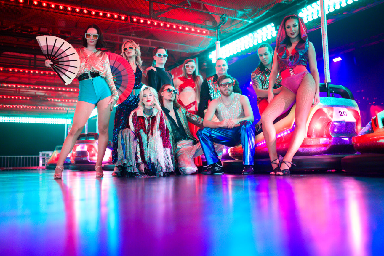 Our performers stand posed in their sequinned costumes, next to brightly lit dodgems